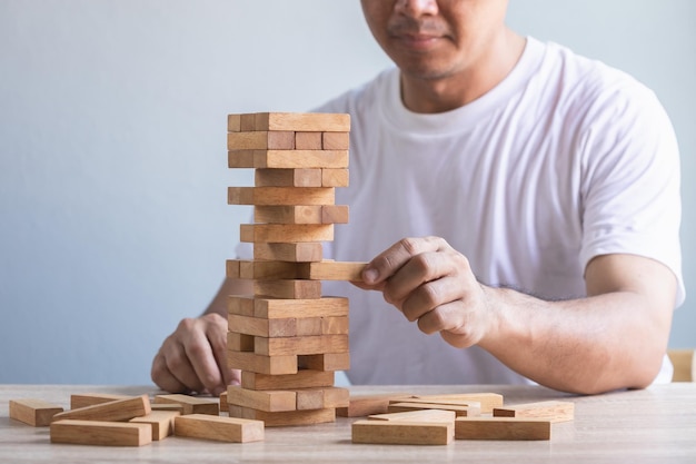 Man die nadenkt over het spelen van het stapeltorenblok houten spel op tafelblad met grijze muurachtergrond