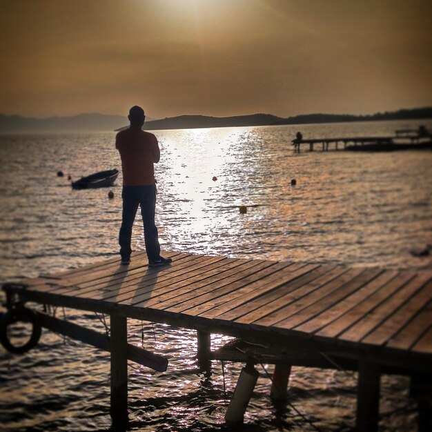 Foto man die op de pier staat bij zonsondergang