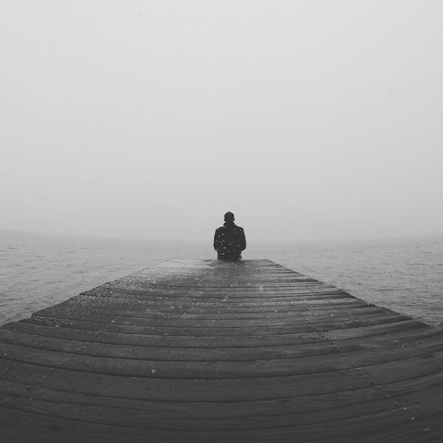 Foto man die op de pier zit en naar de zee kijkt