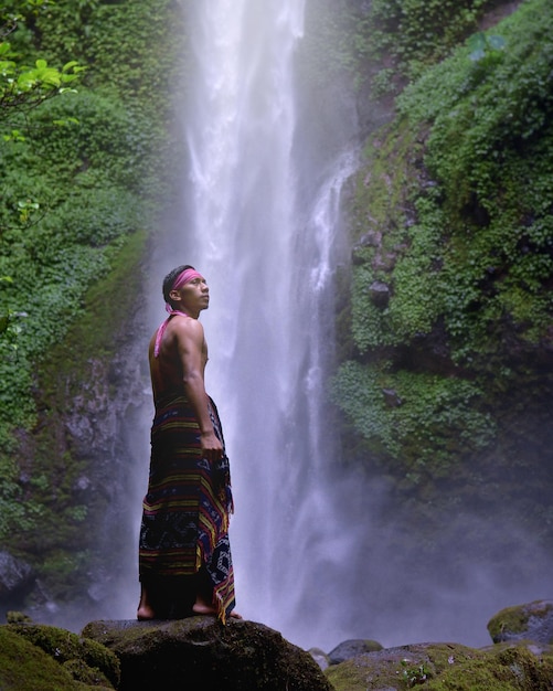 Foto man die op rotsen bij een waterval staat