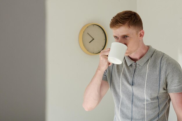 Foto man die 's ochtends koffie drinkt in de kamer met klok die aan de muur hangt