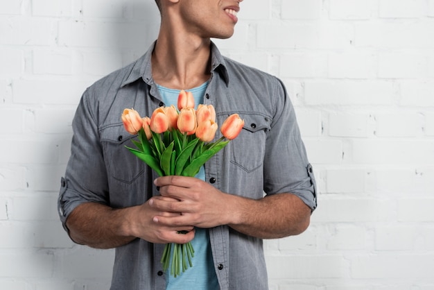 man die tegen een witte bakstenen muur die een tulp boeket in zijn handen