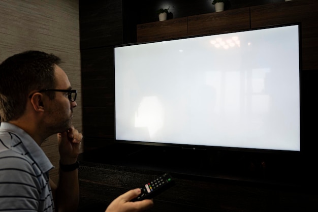 Man die televisie kijkt, plasma flatscreen-tv aanzet en afstandsbediening naar een leeg tv-scherm aan de muur wijst Guy wisselt thuis van kanaal Mockup