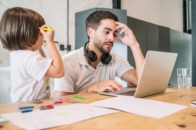 Man die vanuit huis werkt terwijl hij voor zijn zoon zorgt. Blijf thuis. Thuiswerken tijdens covid-19 quarantaine.