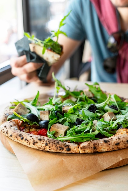 Foto man die veganistische pizza eet met arugula of rucola tofu olijven en tomaten close-up vegetarisch eten