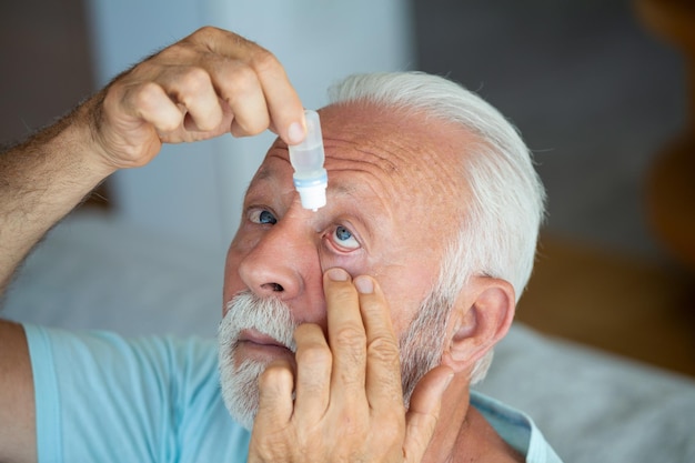 Foto man die vloeibare druppels in zijn oog stopt om gezichtsproblemen op te lossen senioren die oogdruppels gebruiken om zijn oogpijn te genezen visie- en oogheelkundige geneeskunde senioren met grijs haar die oogdruppen gebruiken
