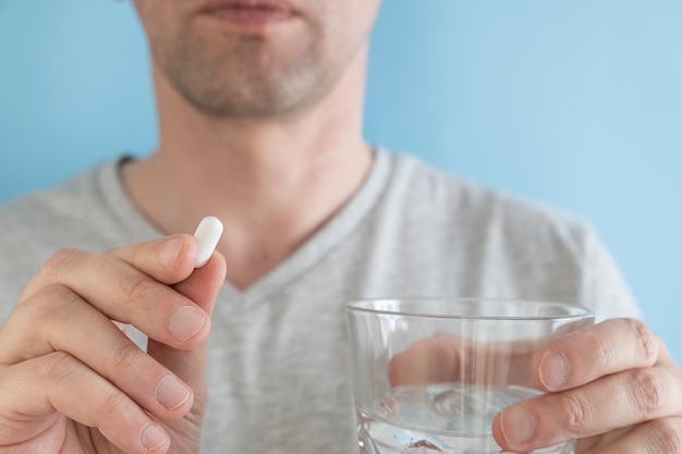 Man die witte pil van statinegeneeskunde neemt om hoog cholesterol te behandelen met een glas water op blauwe achtergrond