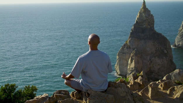 Man die yoga-ontspanning beoefent aan de rand van de oceaanklif Zorgeloze man die binnen mediteert