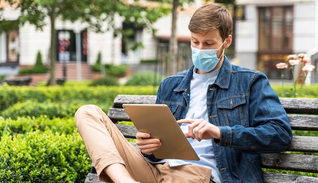 Foto man die zijn tablet controleert terwijl hij een medisch masker draagt