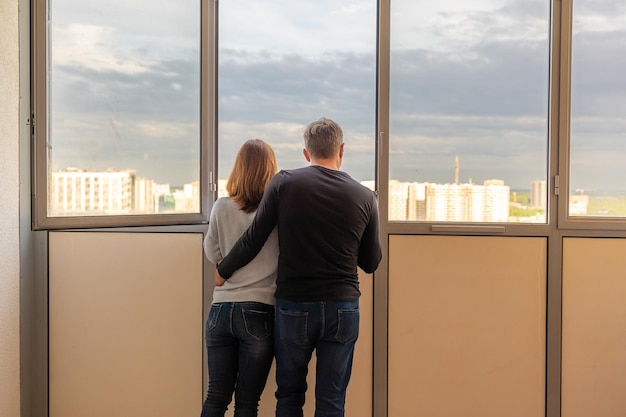 Man die zijn vrouw knuffelt Jong stel dat in een nieuw appartement gaat wonen Mensen kijken uit het raam naar nieuwe huizen