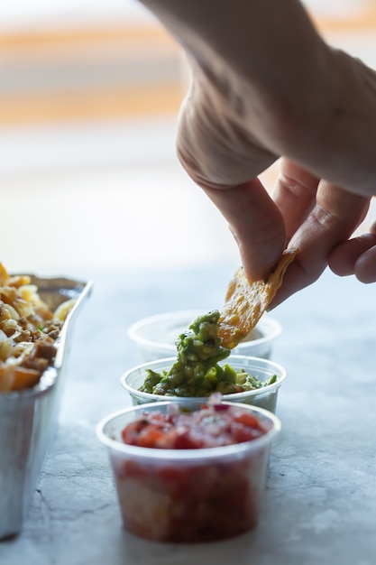 A man dips nachos in green guacamole sauce. Mexican food