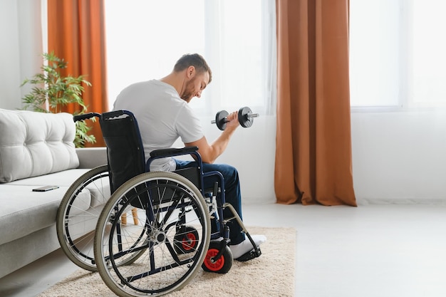 Человек-инвалид Спорт для инвалидов Мужчина в инвалидной коляске с гантелями в руках Мужчина с гантелями в руках Отец-инвалид Занимается спортом в квартире Концепция здоровья Здоровый образ жизни