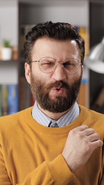Man disgust, abomination, FU, auch emotion. Vertical view of bearded male teacher or businessman with glasses looking at camera and his face is distorted in disgust. Medium shot