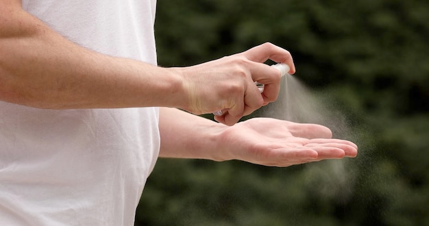 Man disinfecting his hands with sanitizer outdoors in city. Healthcare.