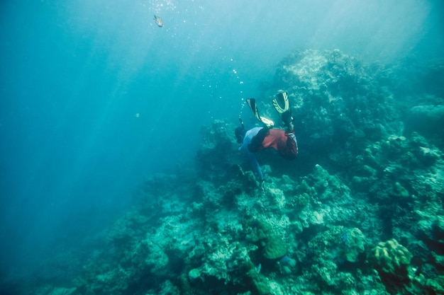 海で魚とサンゴ礁の石でシュノーケリングをダイビングする男