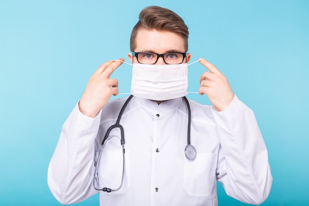 Photo man doctor puts on medical mask on blue wall. coronavirus, covid-19 and pandemic concept.