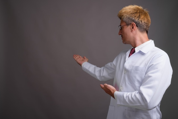 Man doctor with blond hair against gray wall