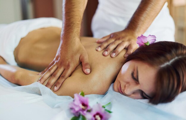 Man does massage to the young woman in white towel indoors