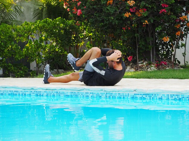 Man does a press exercise near the swimming pool. Side view.