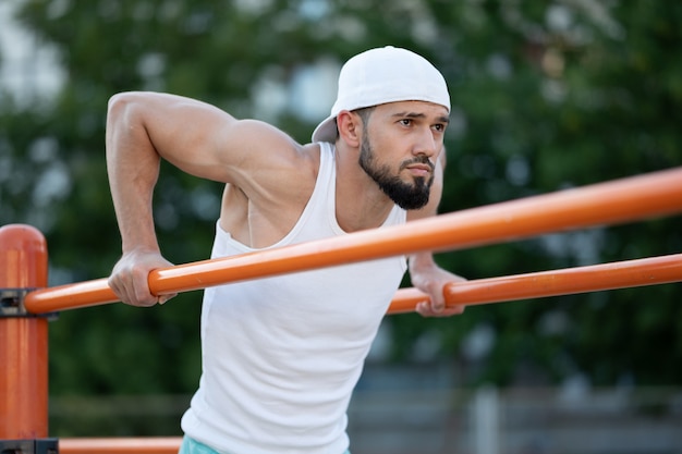 A man does push-UPS on the bars on the street at the day