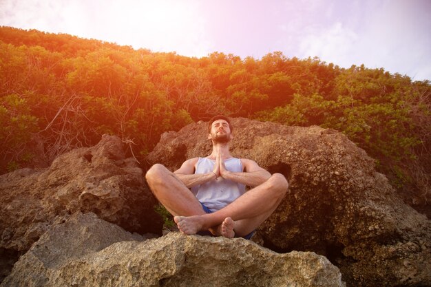 A man does yoga at sunset on the rocks