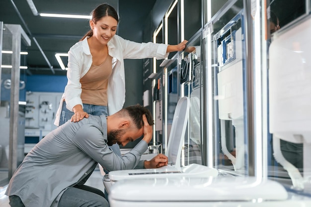 Man doet alsof hij zich slecht voelt op het toilet Vrouw en man zijn in de winkel met goederen voor het huis