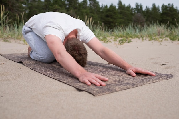 Foto man doet kind pose in yoga op het strand