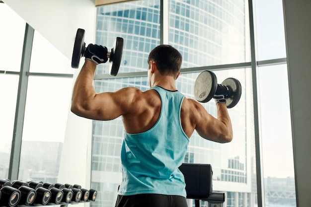 Man doet oefening met halter in de sportschool foto van een sexy gespierde man in sportkleding en een goede lichaamsbouw op grijze achtergrond kracht en motivatie sport fitness doel