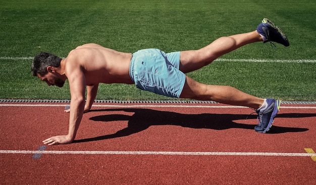 Man doet push-ups oefening op stadion fitness gym buiten gespierde atletische man opleiding sport mannelijke kracht en macht sportman in plank atleet push-ups trainen zijn kernspieren