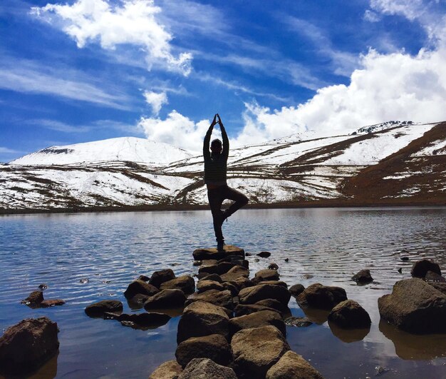 Foto man doet yoga op een rots in een meer tegen de lucht