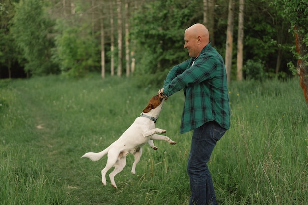 男と犬の友情。男は牧草地でジャックラッセルテリア犬を演じます。