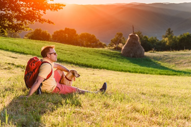 Man and dog sitting on a mountain meadow and enjoying sunset