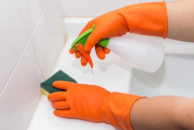 Человек делает хозяйственные работы в ванной дома, умывальник и смеситель с распылительным моющим средством