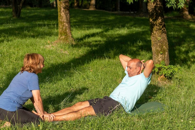 妻の助けを借りてクランチをしている男性は、自然に囲まれて健康で健康になります