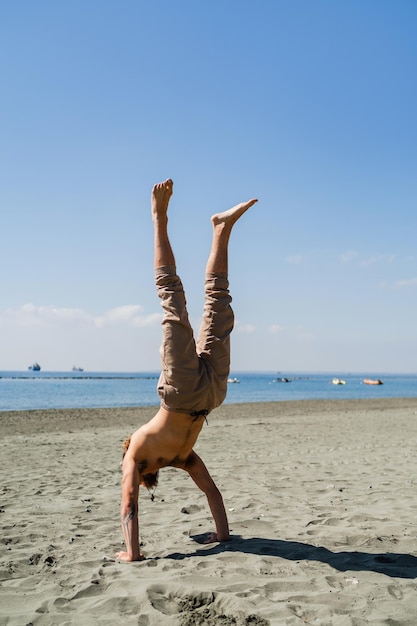 砂浜で強さとバランスのために逆立ちをしている男性