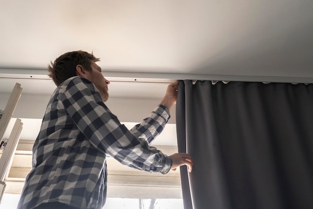 Мужчина, работающий по дому, прикрепляет перила и вешает шторы дома