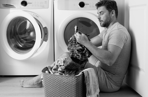 man doing laundry at home near washing machine husband man doing laundry at home sexy guy washer putting clothes in the washing machine household concept washer and dryer laundromat