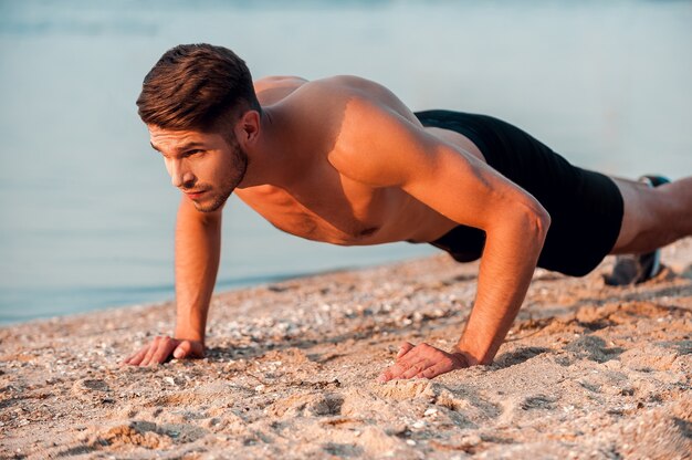 Man doing push-ups. Handsome young muscular man doing push-ups at the riverbank