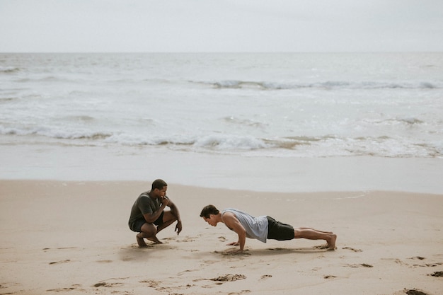 Photo man doing pushups with a trainer at the beach