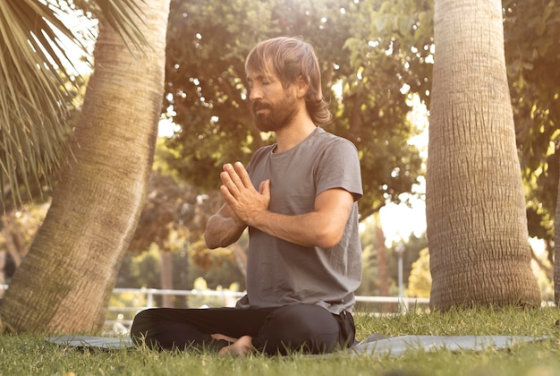 Foto uomo che fa yoga sull'erba all'aperto