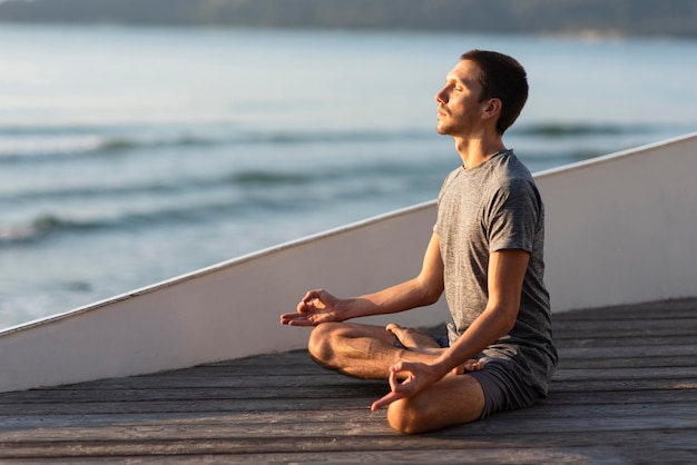 Foto uomo che fa yoga fuori vicino al mare