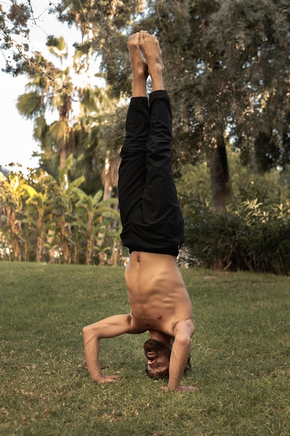 Foto uomo che fa yoga stando in piedi sulla sua testa sull'erba