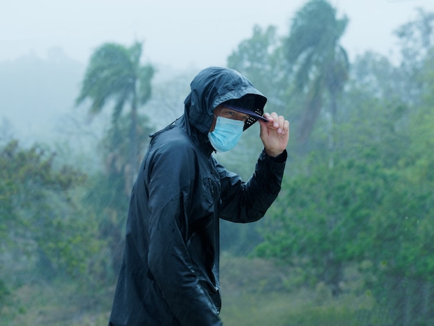 Man draagt gezichtsmasker en regenjas onder zware tropische regen. Tropische omgeving.