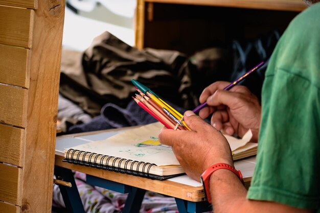 Man drawing on a notebook and holding pencils on a table in a converted van