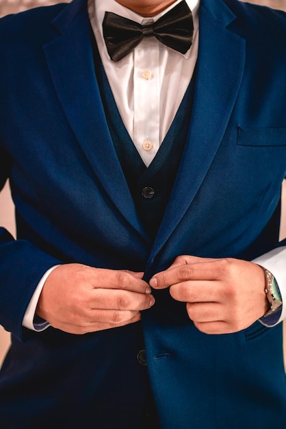Мужчина в синем костюме и галстуке-бабочке завязывает костюм