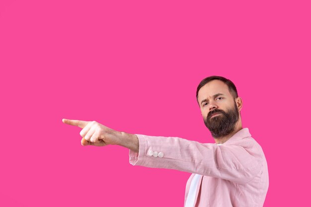 A man dressed in a pink jacket indicates the direction on a pink isolated background