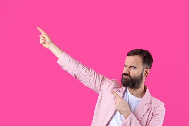 A man dressed in a pink jacket indicates the direction on a pink isolated background