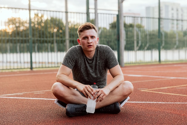 Man dressed in sportswear after tired exhausting trainingexercises sitting at court floor outside