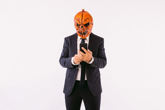 Man dressed in a suit jacket, blue tie and Jack-o-lantern pumpkin mask, staring at his mobile phone, like crazy. Halloween and carnival celebration concept.