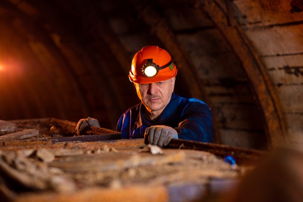 Foto uomo vestito con una tuta da lavoro e un elmetto all'interno di una miniera